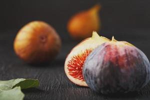 Juicy figs on a dark background, pulp of fig slices with seeds close-up. A group of purple, green fetus and green leaf on a black substrate with a dark background. Soft contrast photo