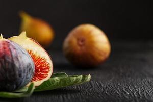 Juicy figs on a dark background, pulp of fig slices with seeds close-up. A group of purple, green fetus and green leaf on a black substrate with a dark background photo