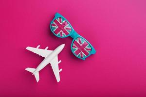 Turquoise sunglasses with United Kingdom flag in lenses on crazy pink background with white airplane. T photo