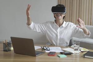 alegre joven mujer de negocios moviendo las manos en el aire mientras usa gafas de realidad virtual en el lugar de trabajo foto