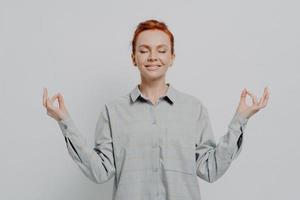 Calm redhaired female in checkered shirt meditating with hands in mudra gesture and eyes closed photo