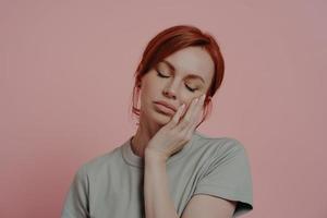 Sleepy tired red-haired woman dozing on hand, falling asleep, isolated over pink background photo
