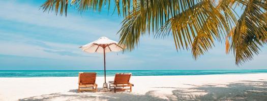 Perfect tropical island, beach resort and hotel background, two sun loungers and umbrella under palm trees near the sea. Summer vacation and beach holiday concept. Tourism landscape if Maldives island photo