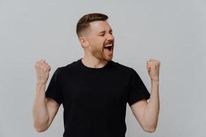 Overjoyed emotional happy man raising clenched fists and screaming while celebrating success photo