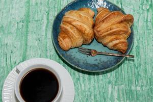 Breakfast food coffee and croissant on isolated green table. photo