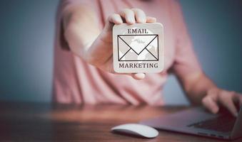 Email marketing concept, Man using Laptop computer and  holding wooden plate  with Email icon and writing Email Marketing text. photo