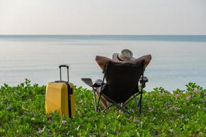 Man sitting on the chair beside suitcase at the beach, vacation, relaxing time concept. photo