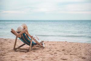 Beautiful young asian woman with hat arm up relaxing on beach chair, Summer happy vacation concept. photo