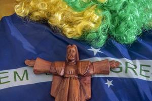 flag of Brazil in a wave filling the frame and a green and yellow wig with a protective saint photo