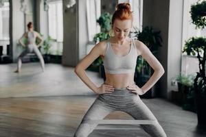 Slender sportive redhead lady performing sit ups with fitness elastic band photo