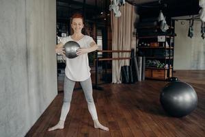 Young fit woman with red hair enjoying barre workout with small fitness ball photo