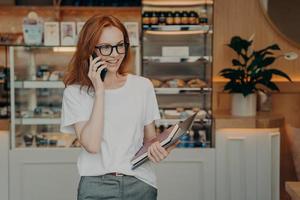 Smiling redhead young woman has telephone conversation enjoys positive talk photo