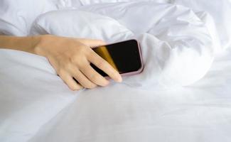 mujer durmiendo en la cama y mano sosteniendo el teléfono móvil. mujer usando teléfono inteligente en el dormitorio. dormido con el teléfono inteligente. Desequilibrio de la vida laboral. sueño poco saludable. adicto a las redes sociales. necesita el concepto de desintoxicación social. foto