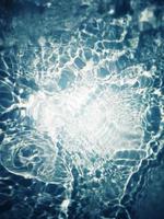 Defocus blurred transparent blue colored clear calm water surface texture with splashes and bubbles. Trendy abstract nature background. Water waves in sunlight with copy space. Blue watercolor shining photo