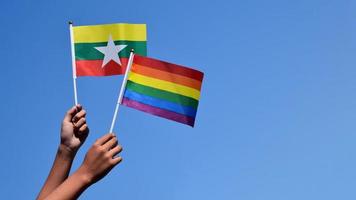 Myanmar and rainbow flags, LGBT symbol, holding in hands, bluesky background, concept for LGBT celebration in Myanmar and around the world in pride month, June, soft and selective focus, copy space. photo