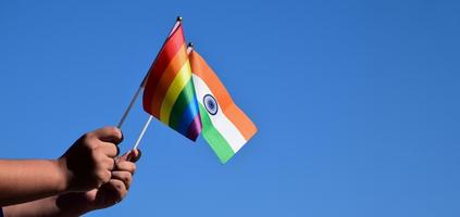 India flag and rainbow flag, LGBT symbol, holding in hands, bluesky background, concept for LGBT celebration in India and around the world in pride month, June, soft and selective focus, copy space. photo