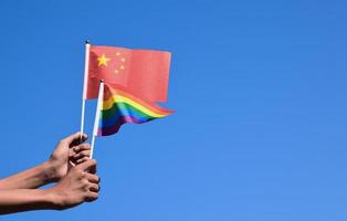 China flag and rainbow flag, LGBT symbol, holding in hands, bluesky background, concept for LGBT celebration in China and around the world in pride month, June, soft and selective focus, copy space. photo