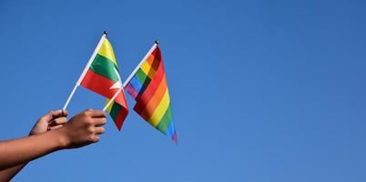 myanmar y banderas del arco iris, símbolo lgbt, tomados de la mano, fondo azul cielo, concepto para la celebración lgbt en myanmar y en todo el mundo en el mes del orgullo, junio, enfoque suave y selectivo, espacio de copia. foto