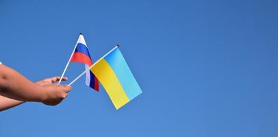 bandera de rusia y bandera de ucrania, sosteniendo en las manos, fondo de cielo azul, concepto para detener la guerra entre rusia y ucrania, enfoque suave y selectivo, espacio de copia. foto