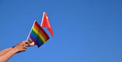 bandera de china y bandera del arco iris, símbolo lgbt, tomados de la mano, fondo azul cielo, concepto para la celebración de lgbt en china y en todo el mundo en el mes del orgullo, junio, enfoque suave y selectivo, espacio de copia. foto