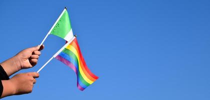 bandera de italia y bandera del arco iris, símbolo lgbt, tomados de la mano, fondo de cielo azul, concepto para la celebración de lgbt en italia y en todo el mundo en el mes del orgullo, junio, enfoque suave y selectivo, espacio de copia. foto