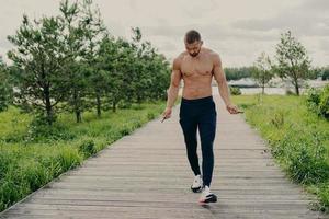 Outdoor shot of muscular active man poses with jumping rope in sportive apparel trains outside, enjoys cardio workout, stays always in good physical shape. Sporty lifestyle, fitness training concept