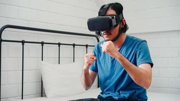 joven asiático usando anteojos simulador de realidad virtual jugando al boxeo en el dormitorio, hombre japonés sintiéndose feliz usando el tiempo de relajación acostado en la cama en casa. los juegos para adolescentes se relajan en el concepto de casa.