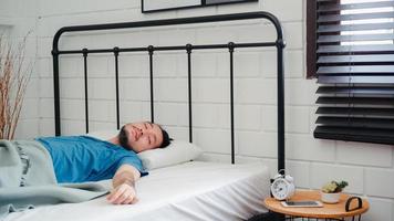 un joven asiático se despierta por la mañana, un hombre se estira después de despertarse en la cama en el dormitorio de su casa. los hombres guapos toman una siesta, se relajan con sueño en el concepto de casa moderna. foto