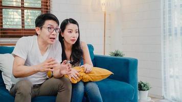 una pareja asiática anima un partido de fútbol frente a la sala de estar de la televisión en casa, una dulce pareja disfruta de un momento divertido mientras se acuesta en el sofá cuando se relaja en casa. pareja de estilo de vida relajarse en el concepto de casa. foto