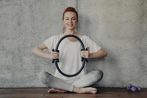 Cheerful fitness woman in active wear sitting in lotus position and exercising with pilates ring photo