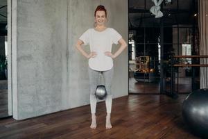 Sportive redhead woman holding mini pilates ball with her knees photo