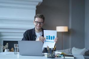 joven empresario alemán sonriente señalando un documento con gráficos durante una reunión en Internet
