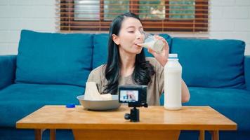 mujeres influyentes asiáticas que usan transmisión de cámara y graban video vlog sobre el beneficio de beber leche y sándwiches para el desayuno en el sofá en la sala de estar en casa para transmitir en línea. foto