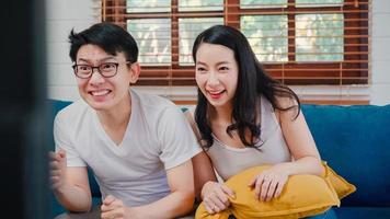 Asian couple cheer football match in front of television living room at home, sweet couple enjoy funny moment while lying on the sofa when relaxed at home. Lifestyle couple relax at home concept. photo