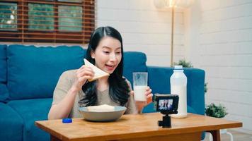 Asian influencer women using camera streaming and recording vlog video about the benefit of drinking milk and sandwiches for breakfast on sofa in living room at home for broadcast online. photo