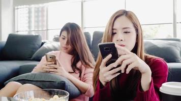 Mujeres asiáticas que usan teléfonos inteligentes y comen palomitas de maíz en la sala de estar en casa, un grupo de amigos compañeros de cuarto disfrutan de un momento divertido mientras están acostados en el sofá. las mujeres de estilo de vida se relajan en el concepto de hogar. foto