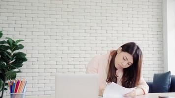 Beautiful young smiling asian woman working laptop on desk in living room at home. Asia business woman writing notebook document finance and calculator in home office. Enjoying time at home concept. photo