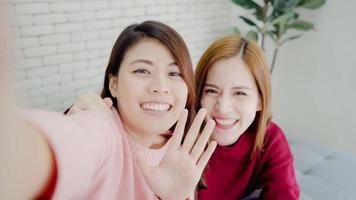 Asian blogger women using smartphone selfie and recording vlog video in living room at home, group of friend enjoy funny moment while lying on the sofa when relax at home. Point of view. photo