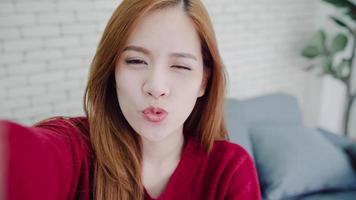 Asian blogger woman using smartphone recording vlog video in living room at home,female enjoy funny moment while lying on the sofa when relax at home. Lifestyle blogger making video at home. photo