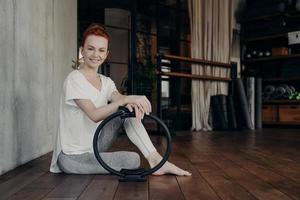 Smiling young sportive woman with pilates ring enjoying workout in fitness studio photo