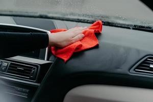 Professional cleaner and car cleaning concept. Unrecognizable man cleans car interior with cloth. Selective focus. Washing auto dashboard with rag photo