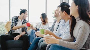 Diversity of young people group team holding coffee cups and discussing something with smile while sitting on the couch at office. Coffee break time at creative office. photo