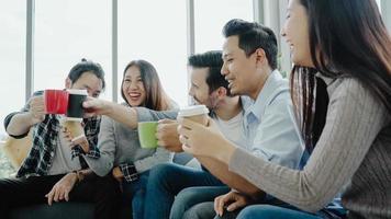 Diversity of young people group team holding coffee cups and discussing something with smile while sitting on the couch at office. Coffee break time at creative office. photo