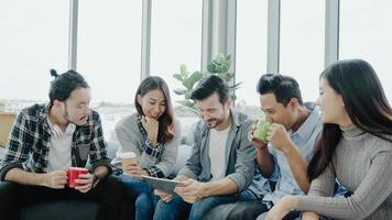 Multiethnic creative team diversity of young people group team holding coffee cups and discussing ideas meeting with tablet sitting on the couch at office. Coffee break time at creative office. photo