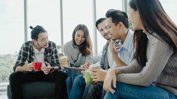 Multiethnic creative team diversity of young people group team holding coffee cups and discussing ideas meeting with tablet sitting on the couch at office. Coffee break time at creative office. photo