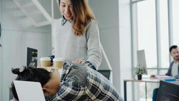 Asian businesswoman giving coffee to her colleague who is working with laptop at office. Group of casually dressed business people discussing ideas in the office. photo