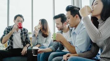 diversidad del equipo del grupo de jóvenes sosteniendo tazas de café y discutiendo algo con una sonrisa mientras está sentado en el sofá de la oficina. tiempo de descanso para tomar café en la oficina creativa. foto