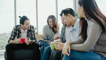 Multiethnic creative team diversity of young people group team holding coffee cups and discussing ideas meeting with tablet sitting on the couch at office. Coffee break time at creative office. photo
