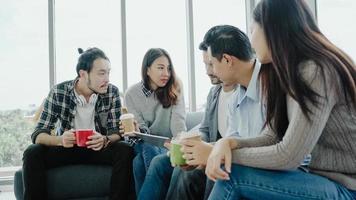 Multiethnic creative team diversity of young people group team holding coffee cups and discussing ideas meeting with tablet sitting on the couch at office. Coffee break time at creative office. photo
