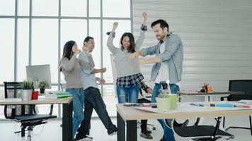 Group of cheerful happy Asian creative business women and men enjoy and having fun dancing while working in her office. Group of casually dressed business people discussing ideas in the office. photo